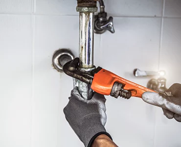 technicien plombier utilisant une grosse clé de serrage pour fixer un système d'écoulement dans une salle d'eau